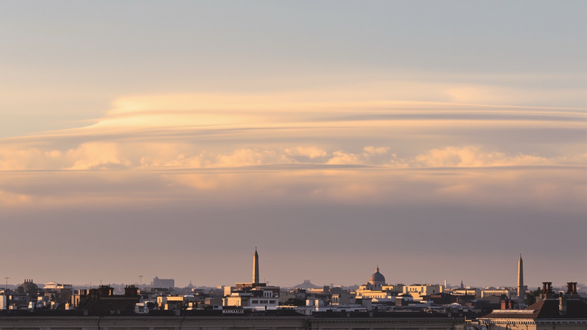 A low level city skyline across the bottom of the frame beneath a large cloudy late afternoon sky