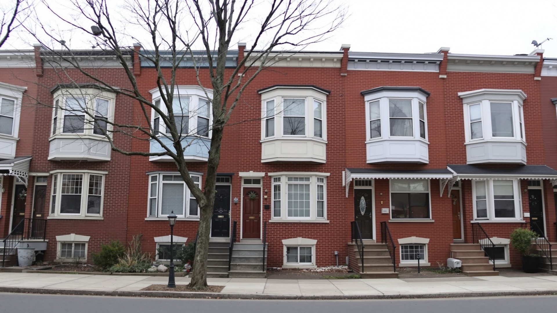 A flat straight-on view of a block of attached brick rowhouses with repeated stoops and bay windows