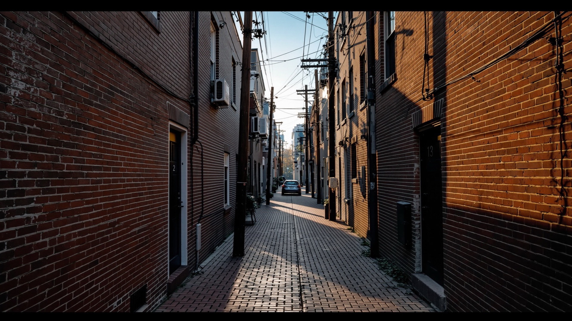 Small two-story brick alley dwellings along a narrow paved service alley behind rowhouses